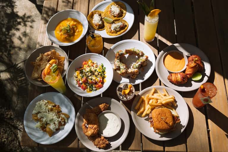 Overhead view of gourmet dishes including soup, pastries, salads, seafood, and beverages on wooden deck