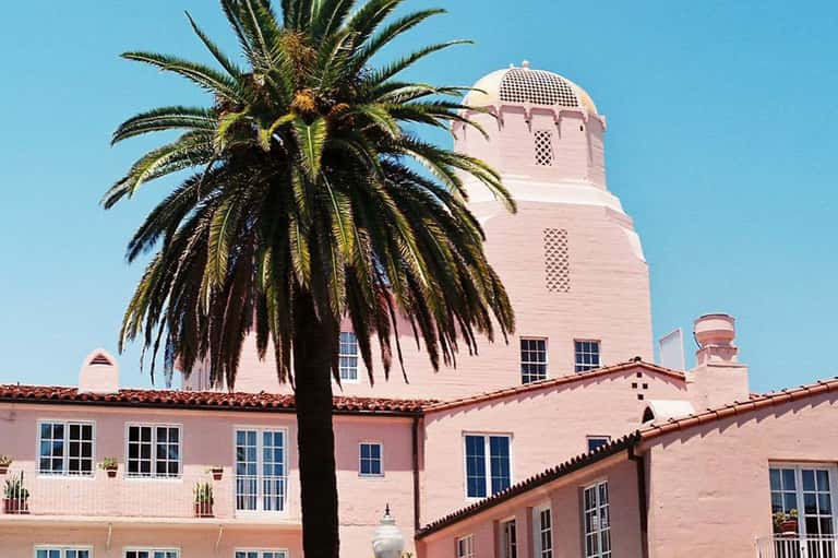 Pink Mediterranean-style building with palm tree and distinctive tower under blue sky