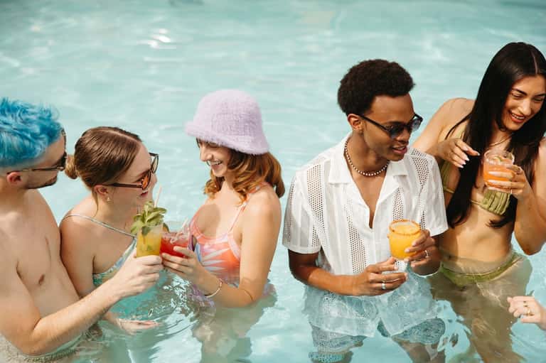 Group of friends enjoying cocktails together in resort pool wearing summer attire