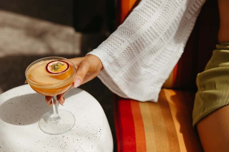 Elegant cocktail with passion fruit garnish held by person in white sweater at outdoor venue