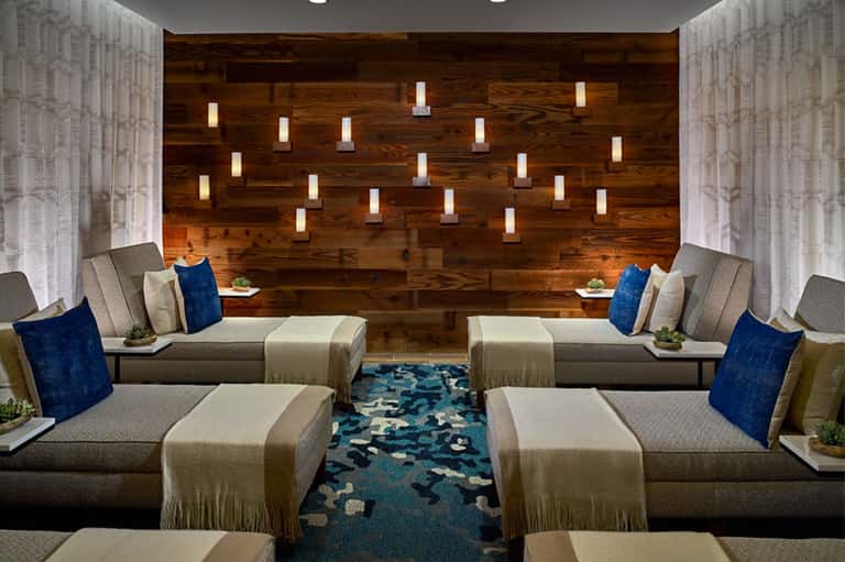 Modern hotel lounge with gray seating, blue pillows, wooden wall, and ambient lighting