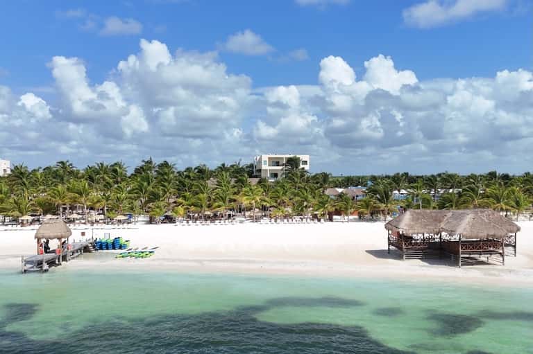 Aerial view of pristine white sand beach with palm trees, thatched structures, and clear turquoise water