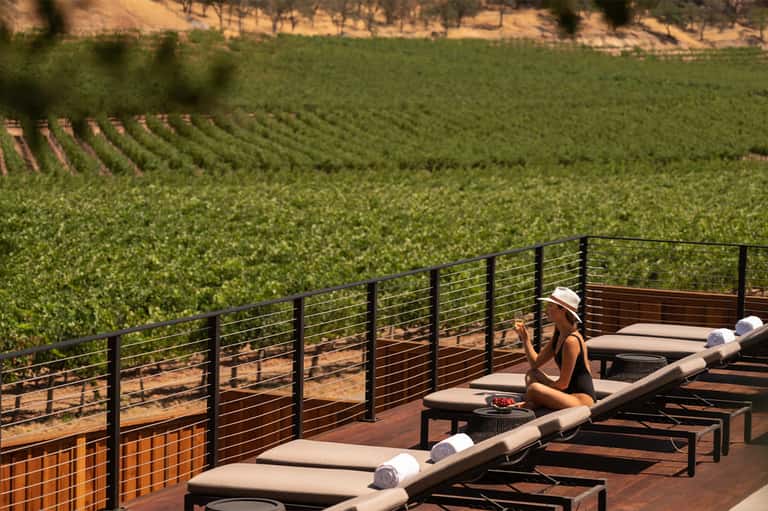 Woman relaxing on vineyard terrace with view of rolling green grapevines below