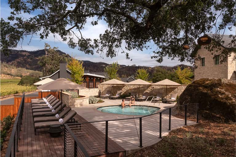 Resort hot tub surrounded by lounge chairs and umbrellas with vineyard hills and stone buildings visible