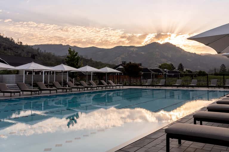 Mountain resort pool at sunset with white cabanas, lounge chairs, and dramatic sky