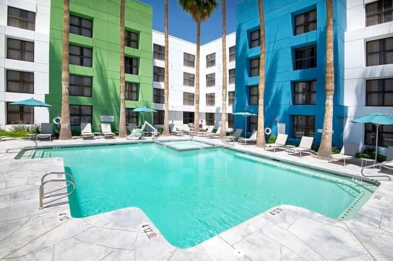 Outdoor pool surrounded by colorful building facades in green, blue, and white with palm trees