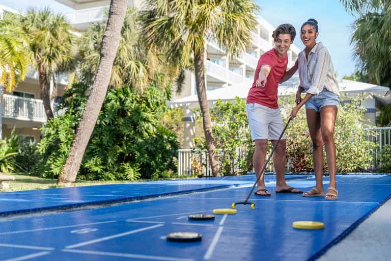 Couple playing mini golf on blue course with palm trees and resort buildings in background