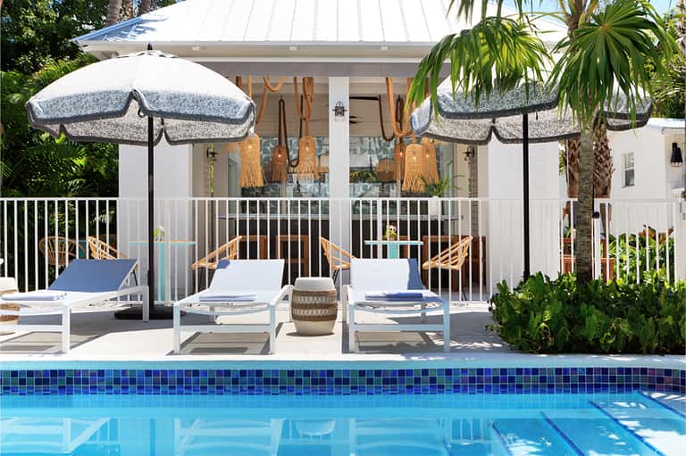 Resort poolside lounge with white umbrellas, loungers, and coastal architectural style building