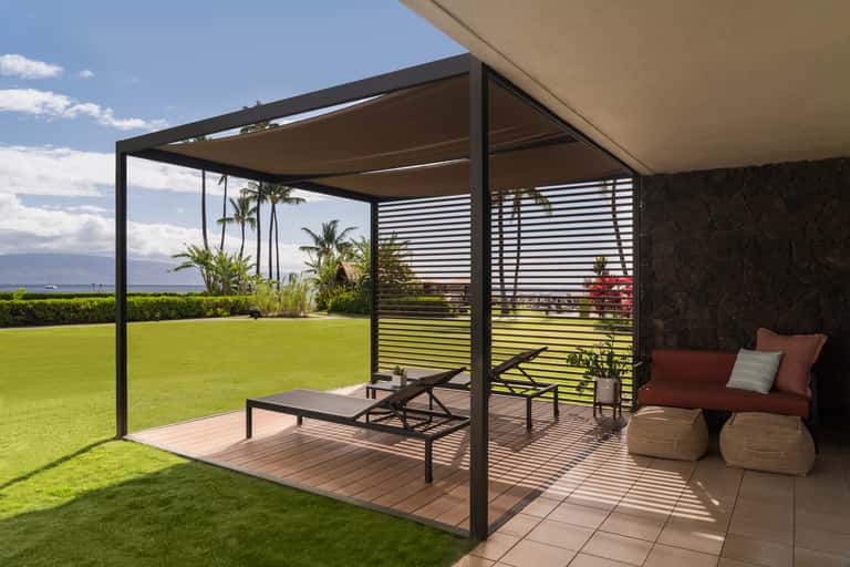 Residential patio with pergola, lounge seating, and manicured lawn overlooking water