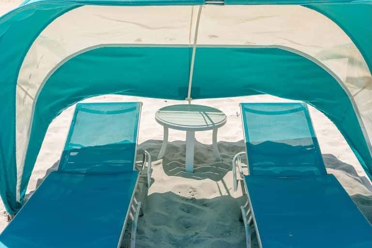 Turquoise beach tent shelter with lounge chairs and small table on sandy beach