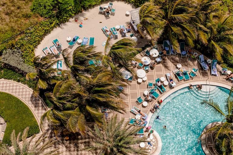 Aerial view of resort pool deck with lounge chairs, umbrellas, and manicured palm trees