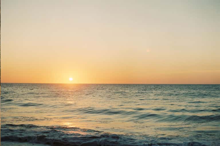 Serene ocean sunset with golden sky reflecting on calm water and gentle waves