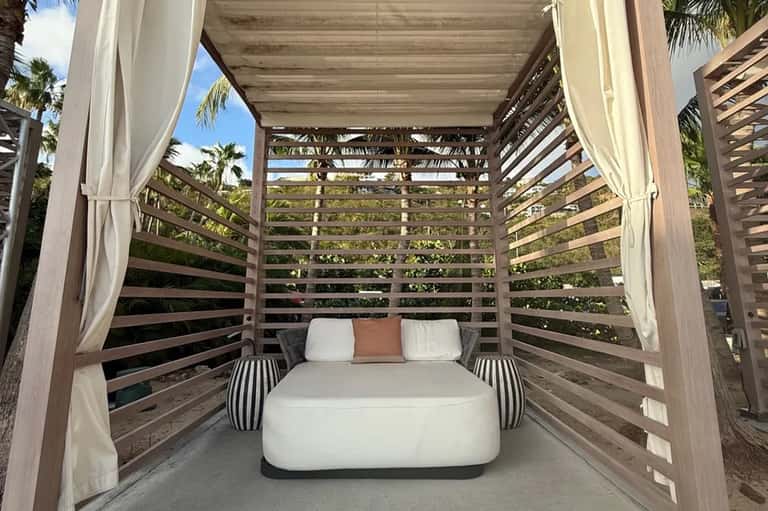 Wooden bed canopy with slatted sides and flowing white curtains on outdoor patio