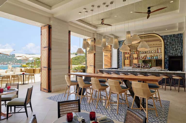 Modern beachside bar and lounge with ocean views, wooden chairs, and pendant lighting
