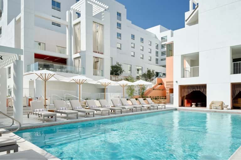 Contemporary hotel pool deck with white umbrellas, lounge chairs, and modern white architecture