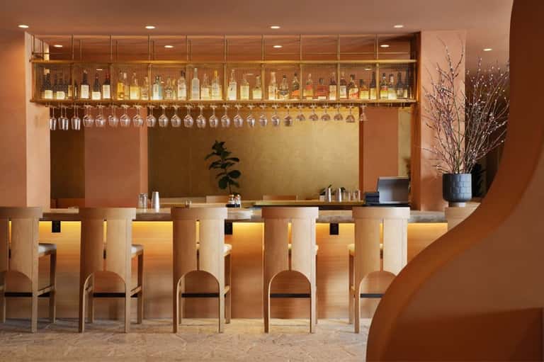 Elegant bar counter with wood paneling, hanging glassware, and bottles displayed on illuminated upper shelf
