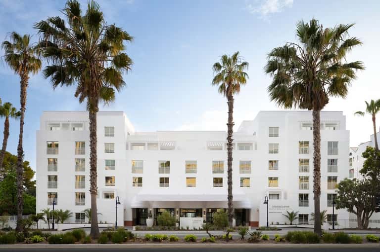 Modern white hotel building with palm trees and minimalist architecture on a tree-lined street