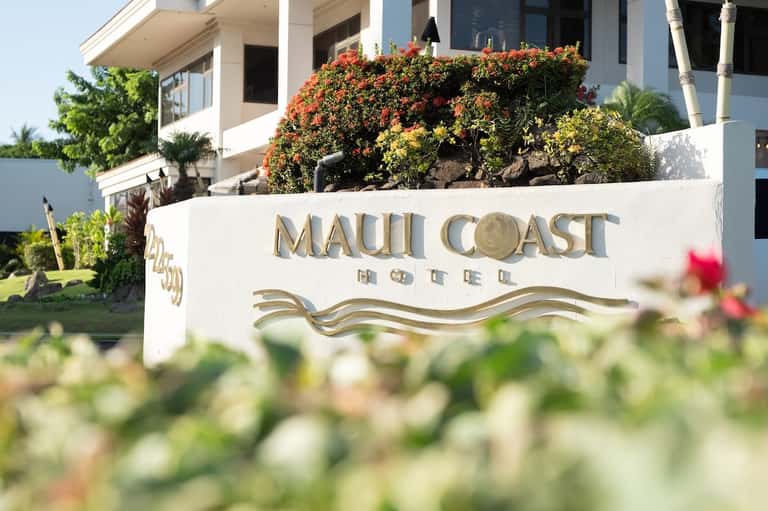 Maui Coast Hotel exterior sign with colorful flowering plants and modern building architecture