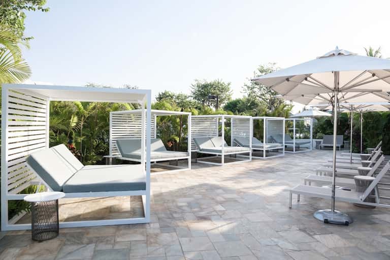 Luxury resort patio with lounge beds, pergola, umbrellas, and lush landscaping