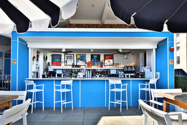 Bright blue outdoor bar with white bar stools and retractable awnings