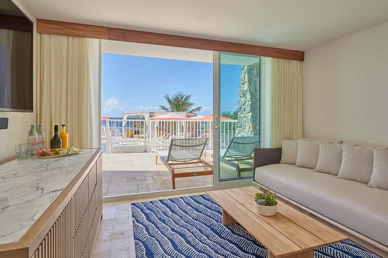 Coastal resort suite with ocean-view balcony, kitchenette, living area, and blue water views