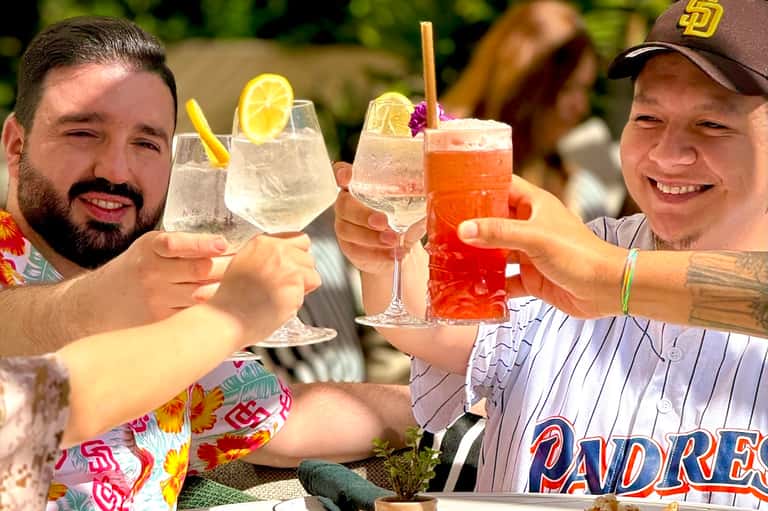 Three men toasting with colorful cocktails outdoors on a sunny day with tropical setting