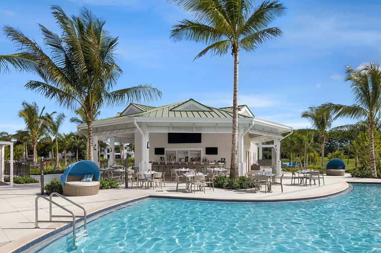 Resort pool with tiki bar pavilion, palm trees, and blue lounge chairs under clear sky