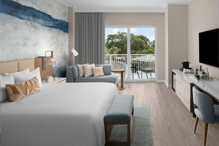 Modern hotel bedroom with balcony view of trees and seating area with artwork