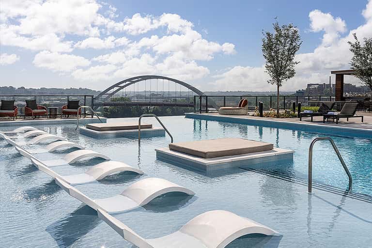Modern rooftop pool with lounge chairs, spa pool, and city skyline views