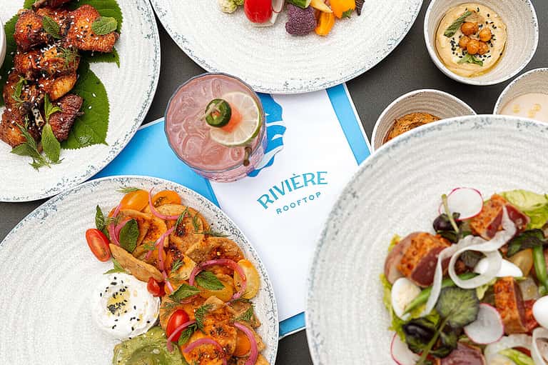 Fine dining rooftop restaurant with plated dishes, cocktail, and city views at Riviere
