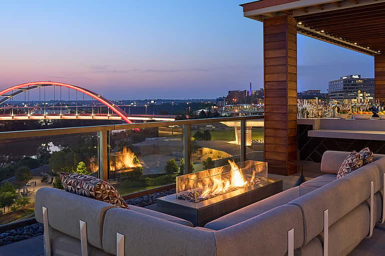 Luxury rooftop terrace with fireplace, seating, and illuminated bridge cityscape view