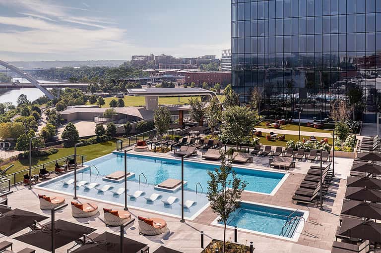 Urban rooftop pool overlooking river valley with modern architecture, lounge chairs, and city views