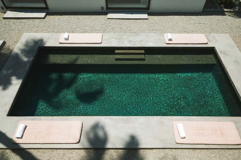 Minimalist rectangular pool with concrete deck and lounge pads adjacent to residence