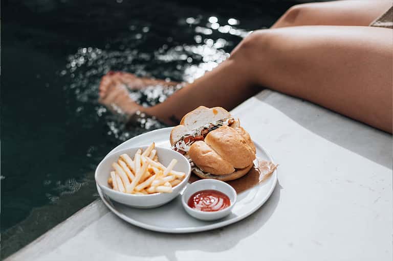 Person enjoying burger and fries by a resort pool with sparkling water