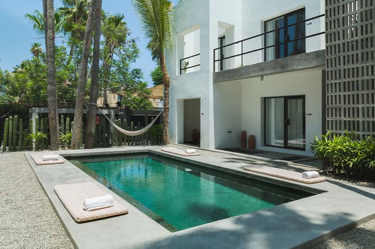 Contemporary poolside villa with turquoise water, palm trees, modern white architecture, and hammock