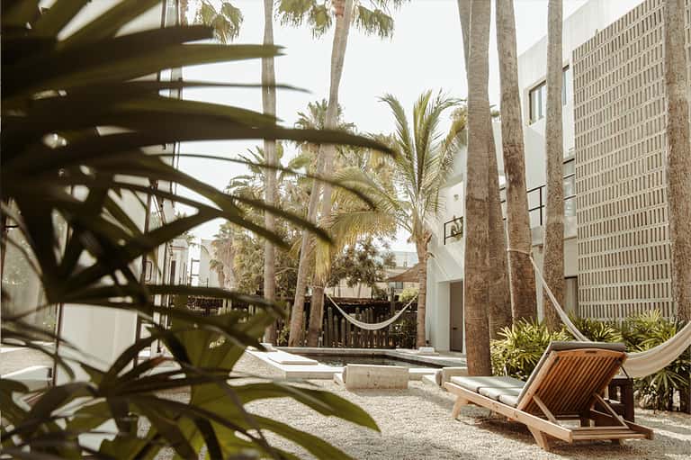Tropical courtyard with palm trees, hammock, wooden lounge chair, and modern white buildings