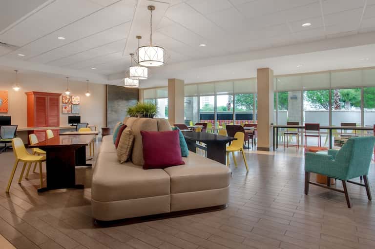 Spacious hotel lobby lounge with colorful accent seating, modern pendant lights, and floor-to-ceiling windows