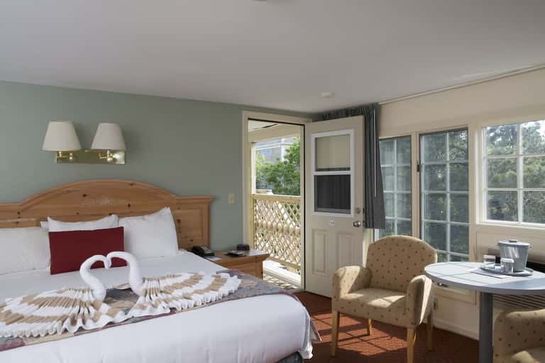 Hotel bedroom with wooden bed frame, mint green accent wall, balcony access, and sitting area with armchair