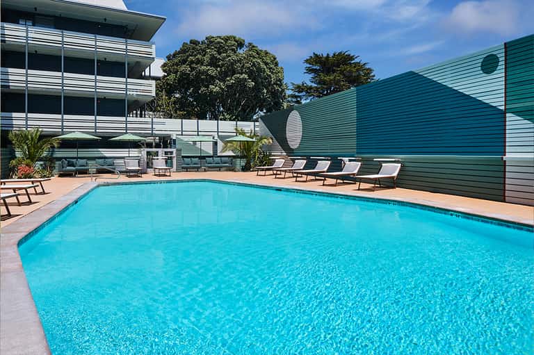 Large turquoise swimming pool with lounge chairs and green modern building architecture