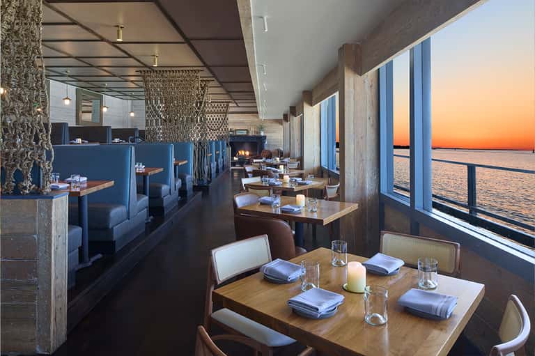 Contemporary restaurant with blue banquettes, wooden tables, and sunset ocean views