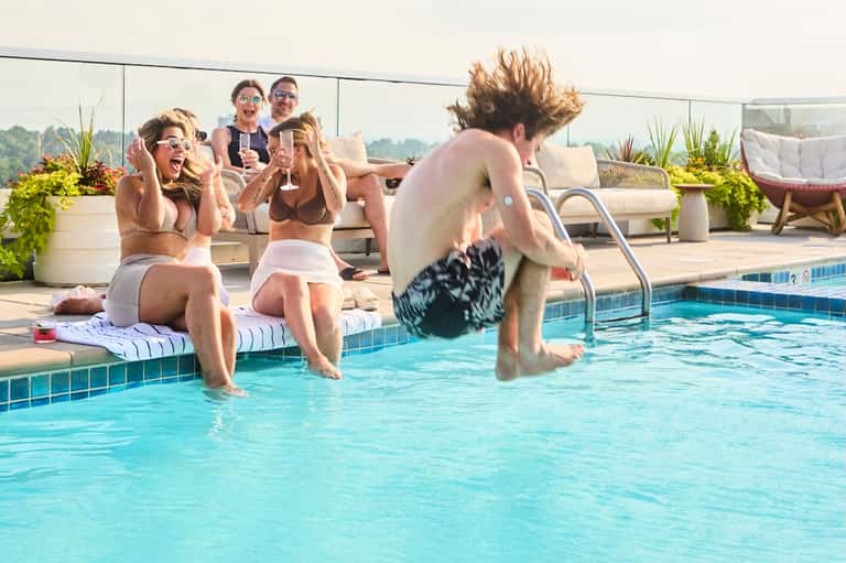 Group of young adults enjoying rooftop pool party with high-rise city views and poolside seating