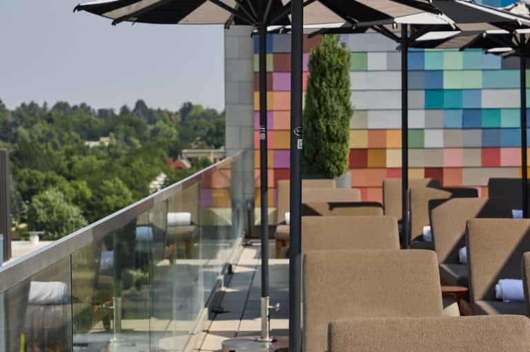 Modern rooftop terrace with colorful grid wall art, black umbrellas, lounge chairs, and forest views