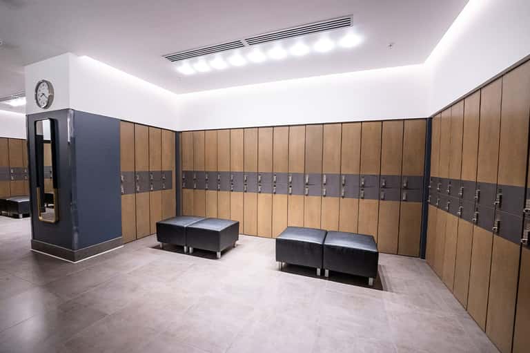 Modern locker room with wooden lockers, bench seating, and bright overhead lighting