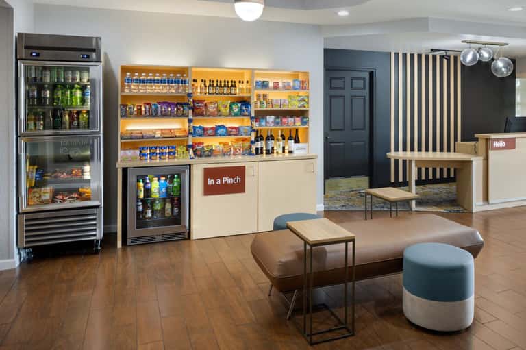 Hotel lobby and convenience store with beverage coolers, snacks, seating area, and check-in desk