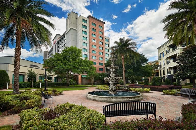 Resort courtyard with fountain, palm trees, manicured landscaping, brick pathways, and multi-story hotel building