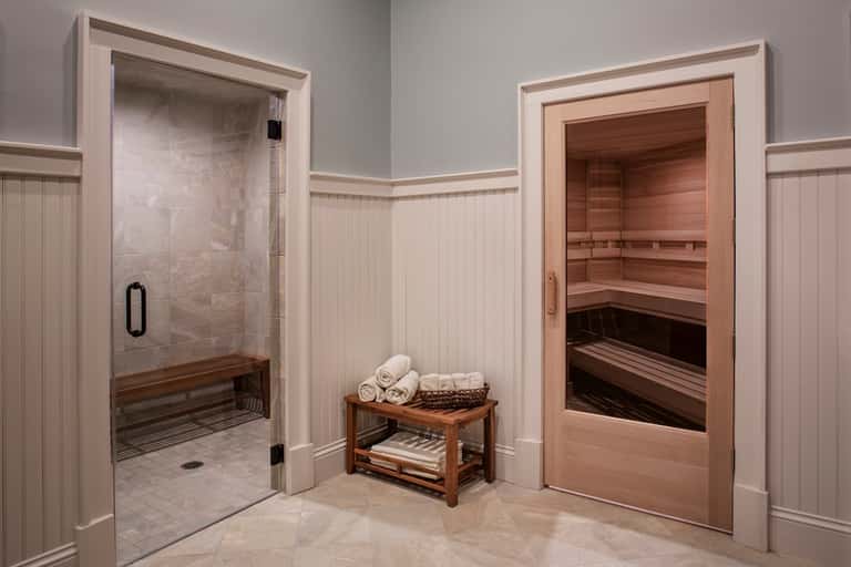 Spa area with steam shower, wooden sauna, white tile floors, and rolled towels on wooden bench