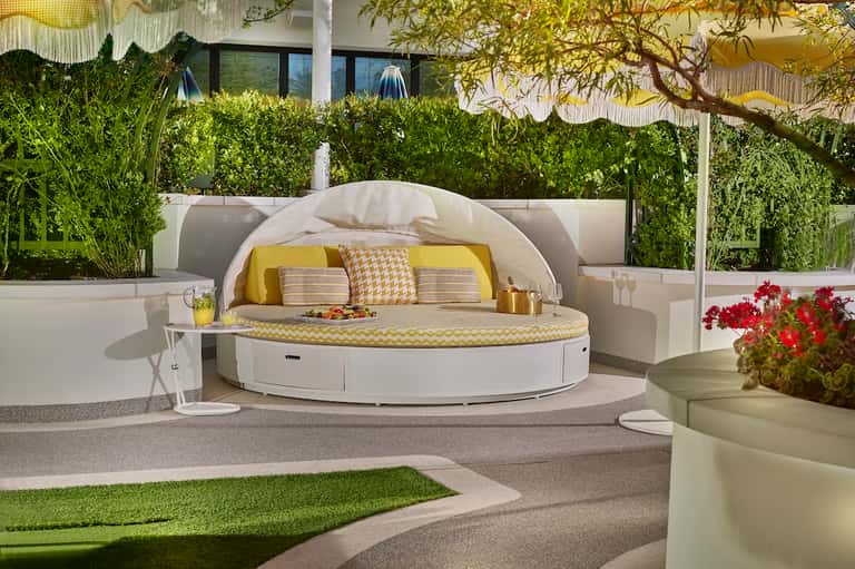 Luxurious round white daybed with yellow cushions on resort terrace with greenery