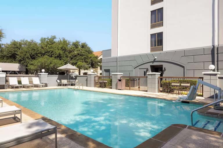 Modern hotel pool with clean blue water, loungers, architecture, and manicured landscaping