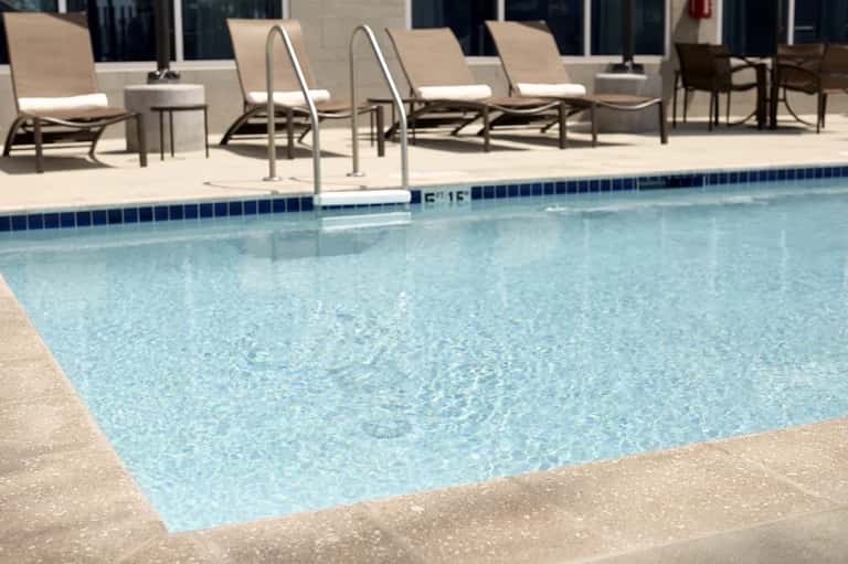 Resort swimming pool with clear blue water, lounge chairs, and umbrellas on sunny day