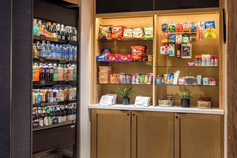 Hotel convenience store with refrigerated beverage cooler and wooden shelving stocked with snacks and amenities